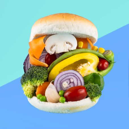 a stack of assorted vegetables including broccoli onion mushroom yellow pepper between an opened burger bun to represent a veggie burger
