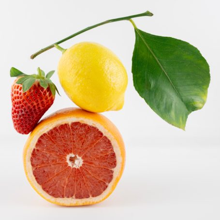 Shot of vibrant fruit arrangement including a lemon with leaf and bright strawberry balanced on top of a cross section of grapefruit