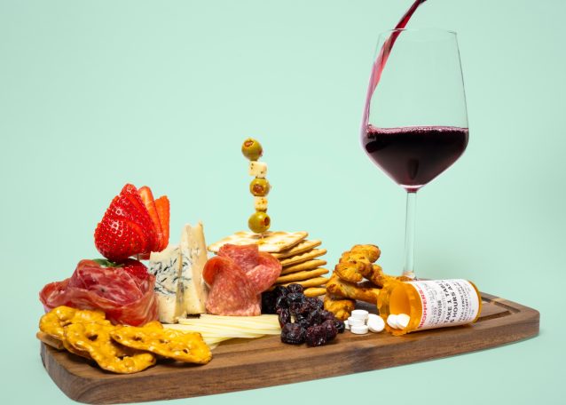 a charcuterie board with blue cheese crackers sliced meats and wine pouring into a wineglass with spilled medication on the side