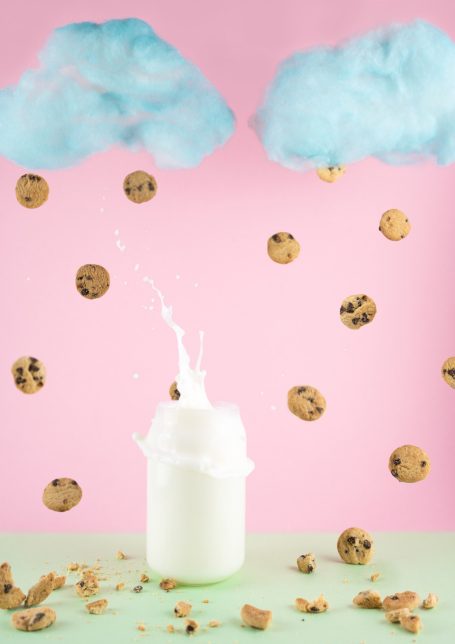 blue puffy clouds with mini cookies raining down and a splash from a cookie landing into a glass of milk